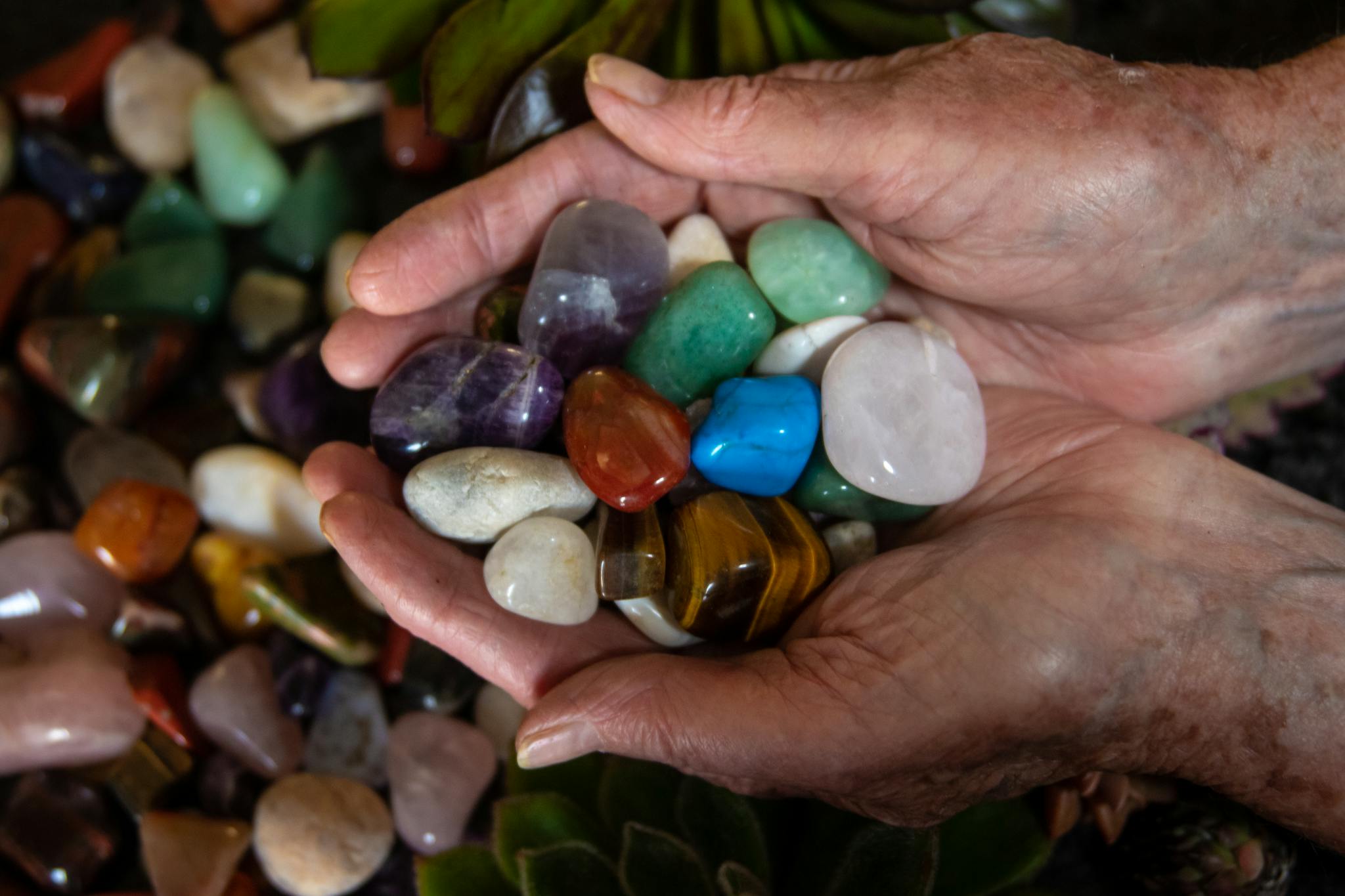 Elderly hands gently cradle various colorful gemstones and crystals.